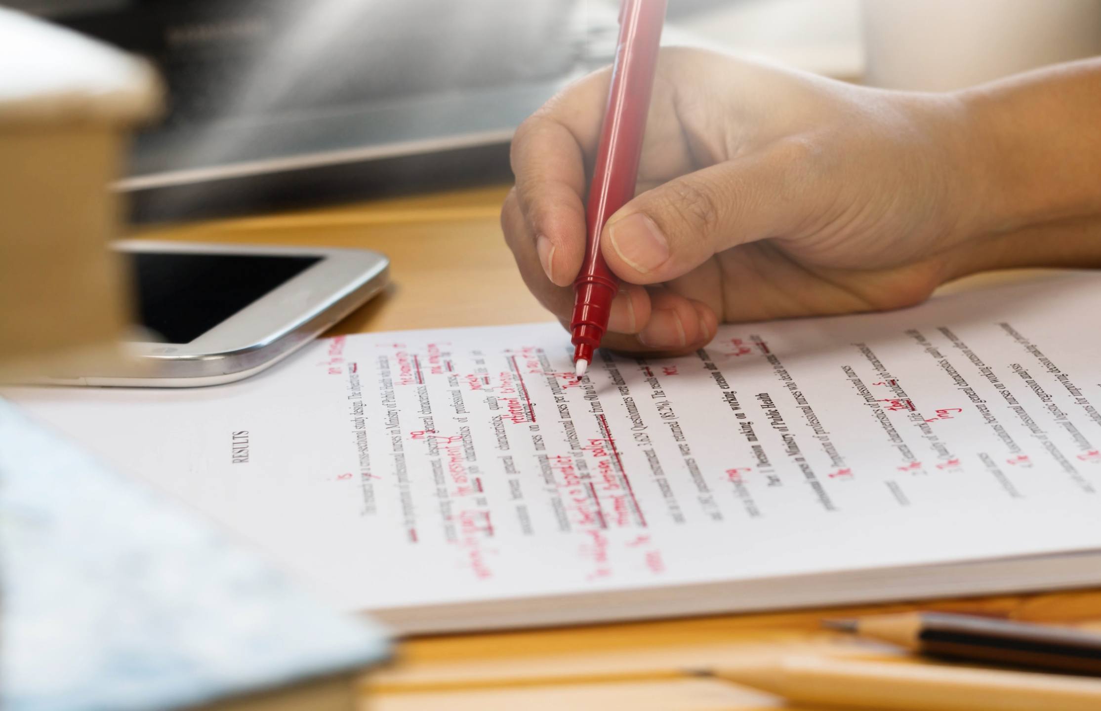 hand holding red pen over proofreading text in office